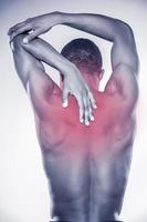 Joint pain. Rear view of young muscular African man touching his neck and elbow while standing against grey background photo