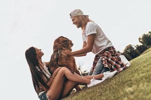 So great to be together. Young modern couple playing with their dog while spending free time in the park photo