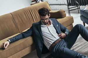 Just relaxing. Top view of handsome young man in full suit resting while sitting on the floor at home photo