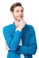 Searching of new creative ideas. Thoughtful young man holding hand on chin and looking away while standing against white background photo