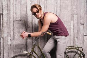 Man on bicycle. Handsome young man in sunglasses sitting on bicycle and looking at camera photo