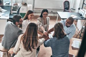 Inspired to work together. Top view of business colleagues holding hands on top of one another in a symbol of unity while working behind the glass wall in the board room photo