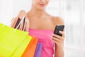 sin tiempo para hablar. imagen recortada de una hermosa joven vestida de rosa sosteniendo bolsas de compras y teléfono móvil foto