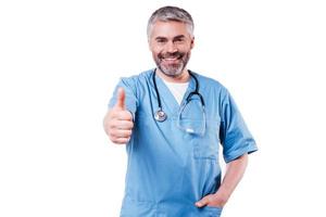 Good news. Happy mature surgeon in blue uniform looking at camera and smiling while standing isolated on white photo