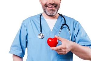 Heart in his hand. Close-up of mature cardiology surgeon holding heart shape toy and smiling while standing isolated on white photo