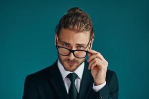 s joven en traje elegante mirando a la cámara y ajustando las gafas mientras está de pie fondo verde foto