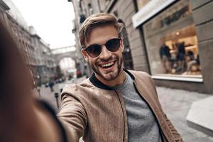 Positively charming. Self portrait of handsome young man in casual wear smiling while standing outdoors photo