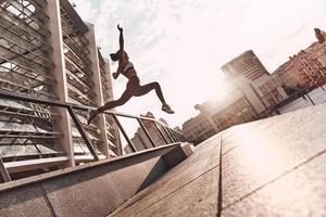 Just flying. Full length of modern young woman in sports clothing jumping while exercising outdoors photo