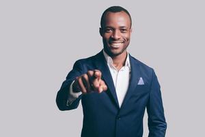 I choose you Handsome young African man in smart casual jacket pointing you and smiling while standing against grey background photo