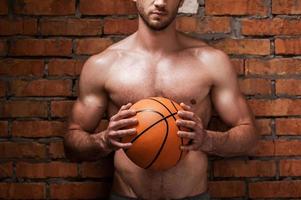 Ready to play ball. Cropped image of young muscular man holding basketball ball while standing against brick wall photo