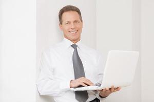 hombre de negocios con computadora portátil. un anciano alegre con camisa y corbata sosteniendo una laptop y sonriendo a la cámara foto