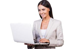 Businesswoman with laptop. Confident young businesswoman in suit working on laptop while standing isolated on white background photo