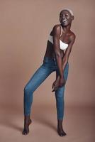 African style. Full length of attractive young African woman looking at camera and smiling while standing against brown background photo