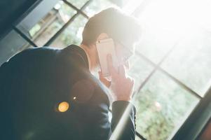 Staying in touch with colleagues. Low angle rear view of confident young man talking on the mobile phone and looking away while standing in front of the big window indoors photo