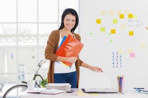 Female assistant. Smiling business woman holding reports and looking at camera photo
