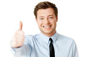 Everything is great Handsome young man in shirt and tie showing his thumb up and smiling while standing isolated on white photo