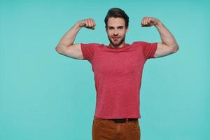 Confident young man in casual clothing showing his biceps and looking at camera photo