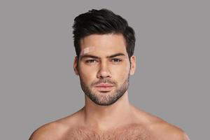 Little injury. Handsome young man with adhesive bandage above eyebrow looking at camera while standing against grey background photo