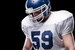 Sport is his everything  American football player looking down while standing against black background photo