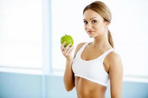 Sport and dieting. Beautiful young woman in sports clothing holding green apple and smiling at camera photo