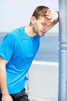 Feeling exhausted after running. Tired young man holding hand on forehead and looking away while standing outdoors photo