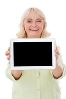 Copy space on her digital tablet. Happy senior woman showing her digital tablet and smiling while standing isolated on white background photo