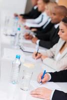 Business conference. Side view of business people writing something in their note pads while sitting in a row photo