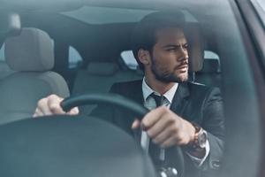 Looking around. Handsome young man in full suit looking away while driving a car photo