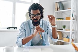 Intelligent young African man in eyewear telling something and looking at camera while working indoors photo