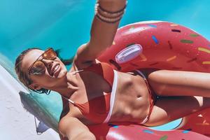 Feeling so carefree. Self portrait of attractive young woman in swimwear smiling while floating on the inflatable ring in the swimming pool photo