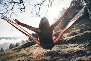 Rear view of young woman keeping arms outstretched while relaxing in hammock outdoors photo