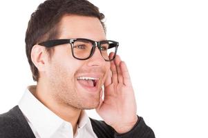 Telling great news. Portrait of handsome young man holding hand near mouth and shouting while standing isolated on white photo