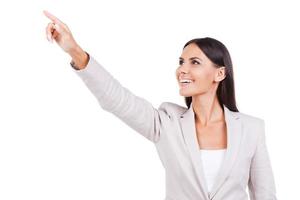 Look over there Curious young businesswoman in suit pointing away and smiling while standing against white background photo