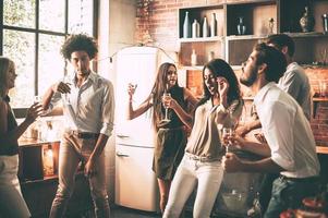 Friends dancing. Cheerful young people dancing and drinking while enjoying home party on the kitchen photo