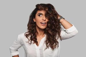 Impossible to resist her. Attractive young smiling woman playing with her hair and looking away while standing against grey background photo