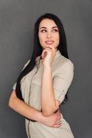 Thoughtful beauty. Thoughtful young woman looking away and smiling while standing against grey background photo