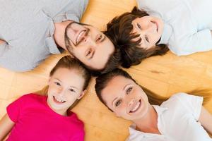 Happy to be a family. Top view of happy family of four bonding to each other heads and smiling while lying on the h floor photo