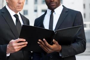 Examining documents. Cropped image of two confident business men looking at the note pad while standing outdoors photo