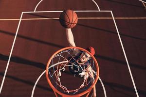 haciendo esfuerzo vista superior del joven en ropa deportiva anotando un slam dunk mientras juega baloncesto al aire libre foto