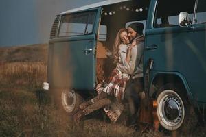 sintiéndose cálido en sus brazos. un joven apuesto abrazando a su bella novia y sonriendo mientras se sienta en una minivan azul de estilo retro foto