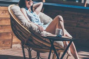 disfrutando de un buen día de verano. imagen recortada de una hermosa joven relajándose en una silla grande y cómoda en la terraza de su casa al aire libre foto