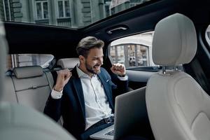 I did it  Handsome young man in full suit gesturing and smiling while sitting in the car photo