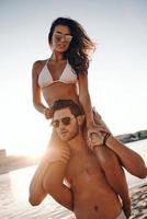 Living at the moment.  Handsome young man carrying his attractive girlfriend on shoulders while standing on the beach photo