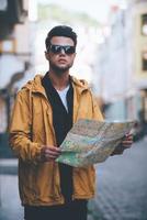 Discovering city. Handsome young man holding map and looking away while standing on the city street photo