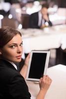 Businesswoman with digital tablet. Rear view of beautiful young woman in formalwear working on digital tablet and looking over shoulder while sitting at the restaurant photo