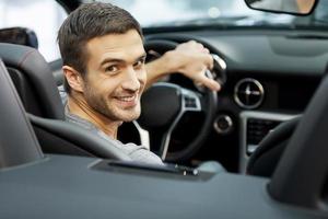 feliz propietario de cabriolet en el concesionario. hombres jóvenes guapos sentados en el asiento delantero del coche mirando a la cámara foto