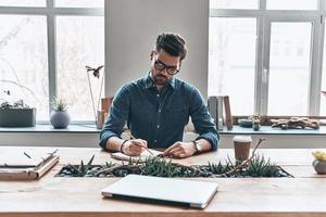 organizando cada minuto. un joven pensativo escribiendo algo en un organizador personal mientras estaba sentado en la oficina foto