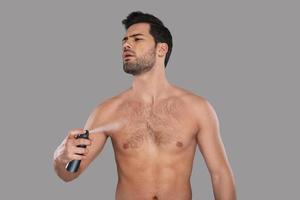Feels good Handsome young man looking away and applying deodorant while standing against grey background photo