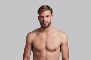 Portrait of confidence. Handsome young man looking at camera and smiling while standing against grey background photo