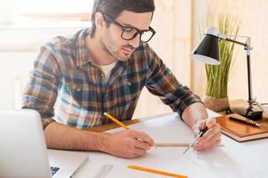 Bringing his ideas to life. Concentrated young man drawing while sitting at his working place photo